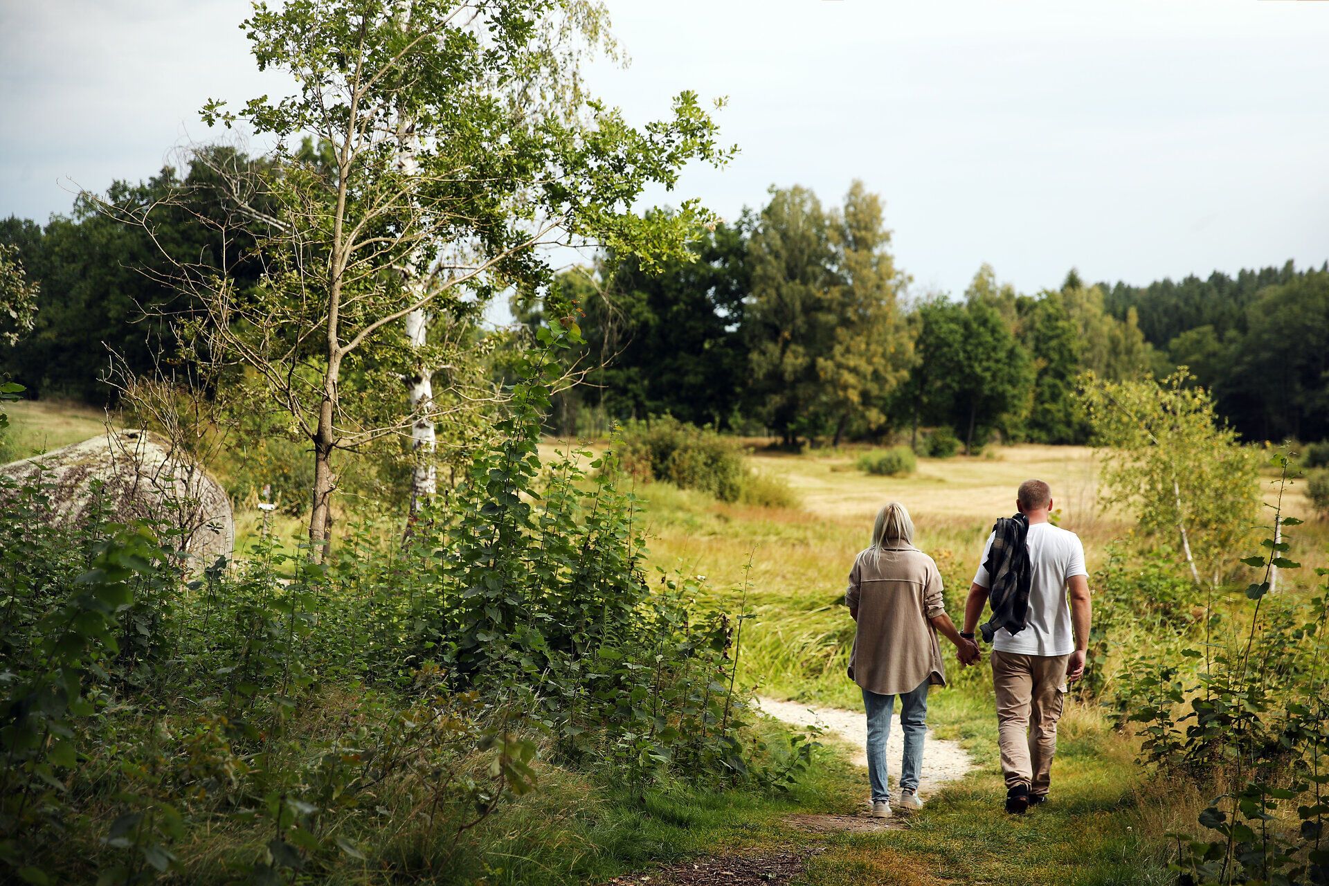 Ein Paar spaziert Hand in Hand neben einem Feld.