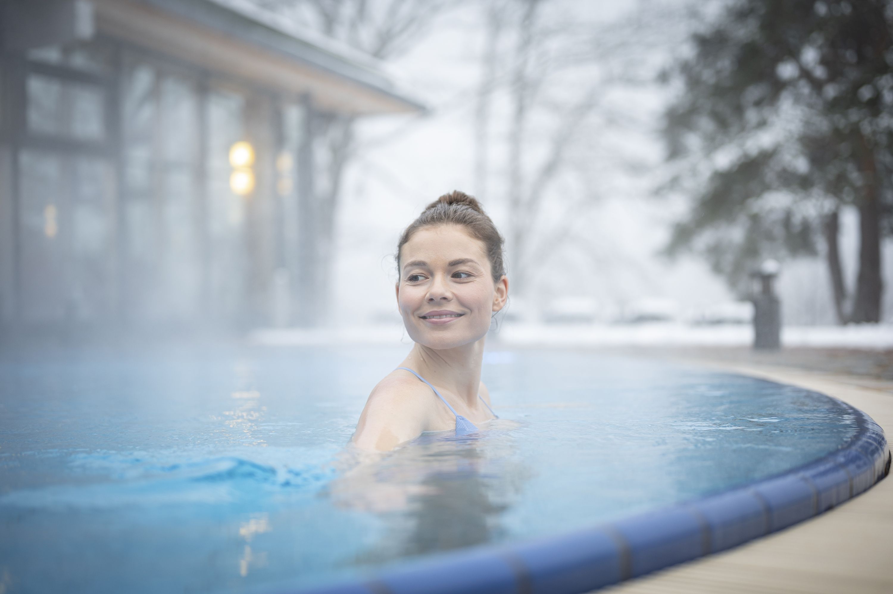 Frau im Außenpool bei kaltem Wetter, umgeben von Dampf.