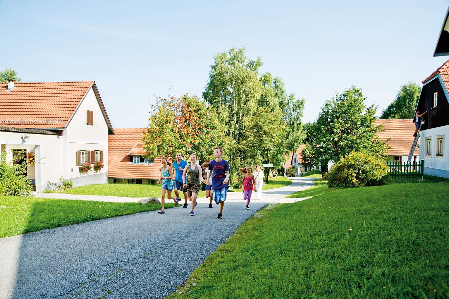 Gruppe von Menschen läuft auf einem Weg in einem Feriendorf mit roten Dächern und grüner Umgebung.