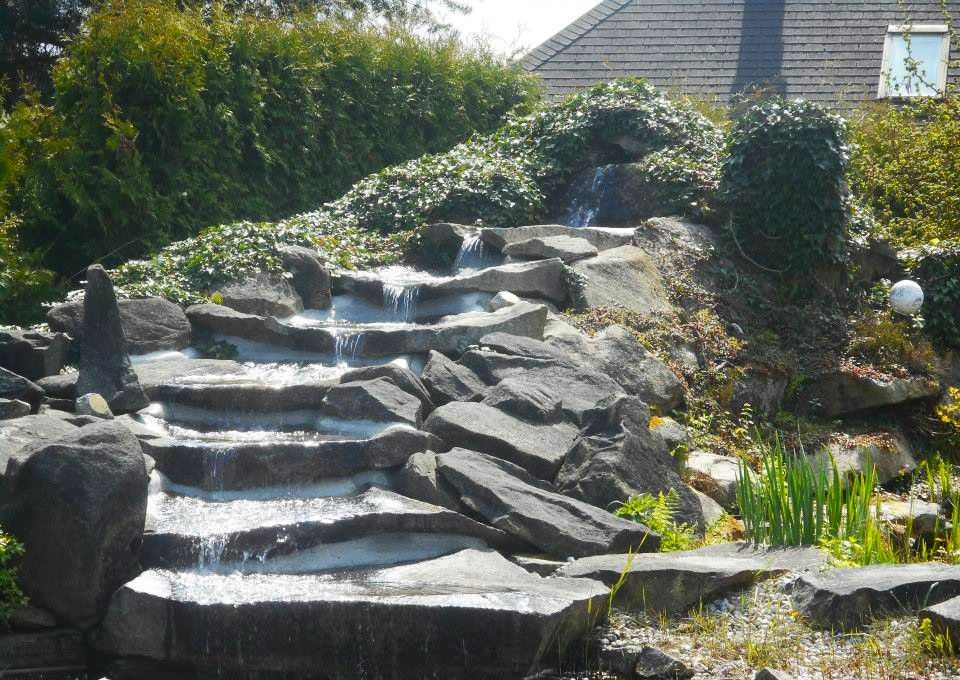 Steinwasserfall in einem Garten mit Pflanzen und Büschen.