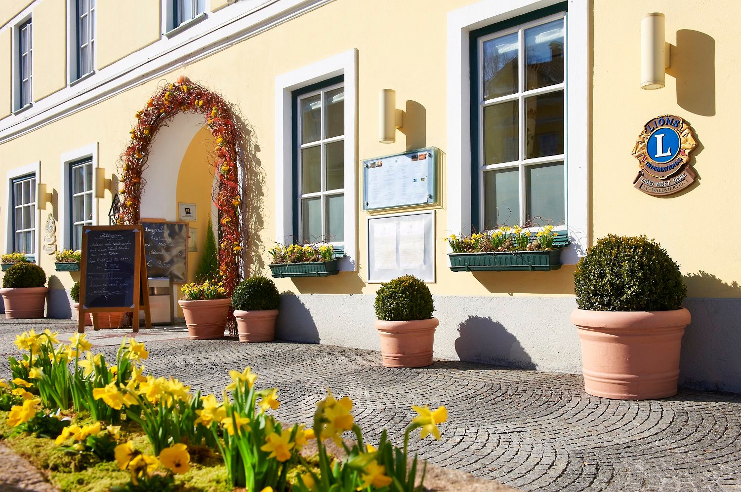 Eingang eines gelben Gebäudes mit Blumen und Schildern.