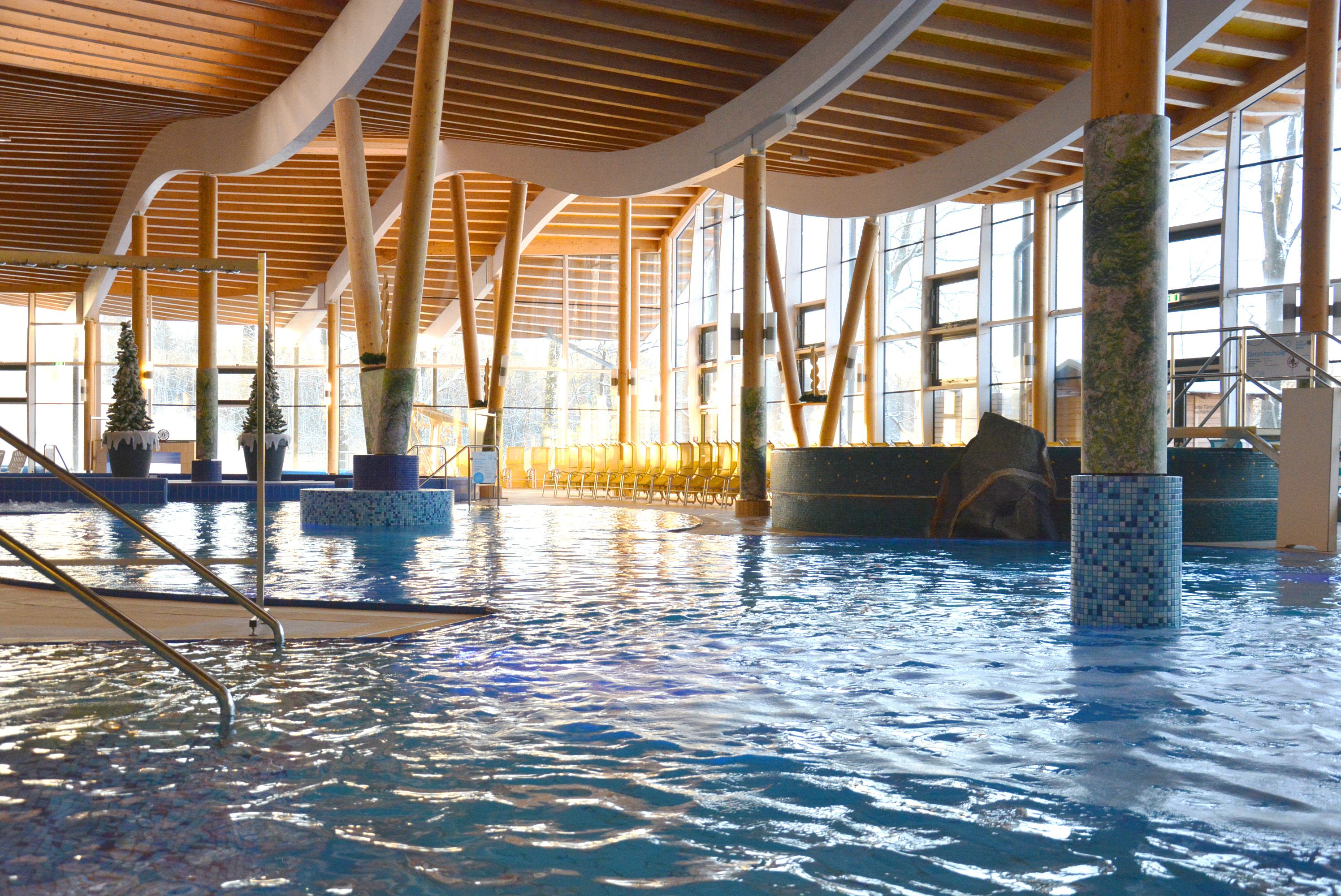 Innenansicht eines modernen Schwimmbads mit Holzsäulen und großen Fenstern.