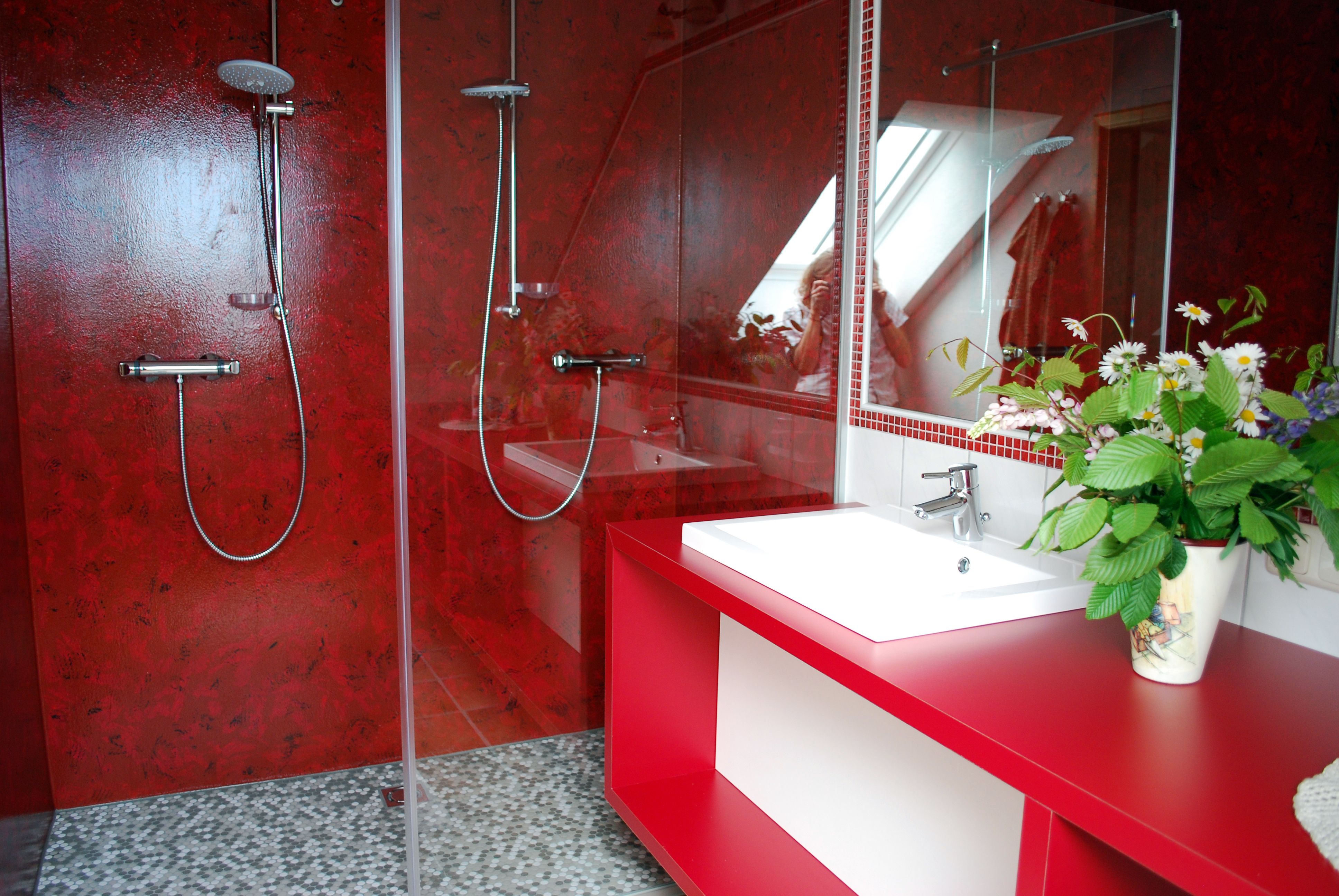 Modernes Badezimmer mit roten Wänden, zwei Duschen und einem Waschbecken mit Blumenarrangement.