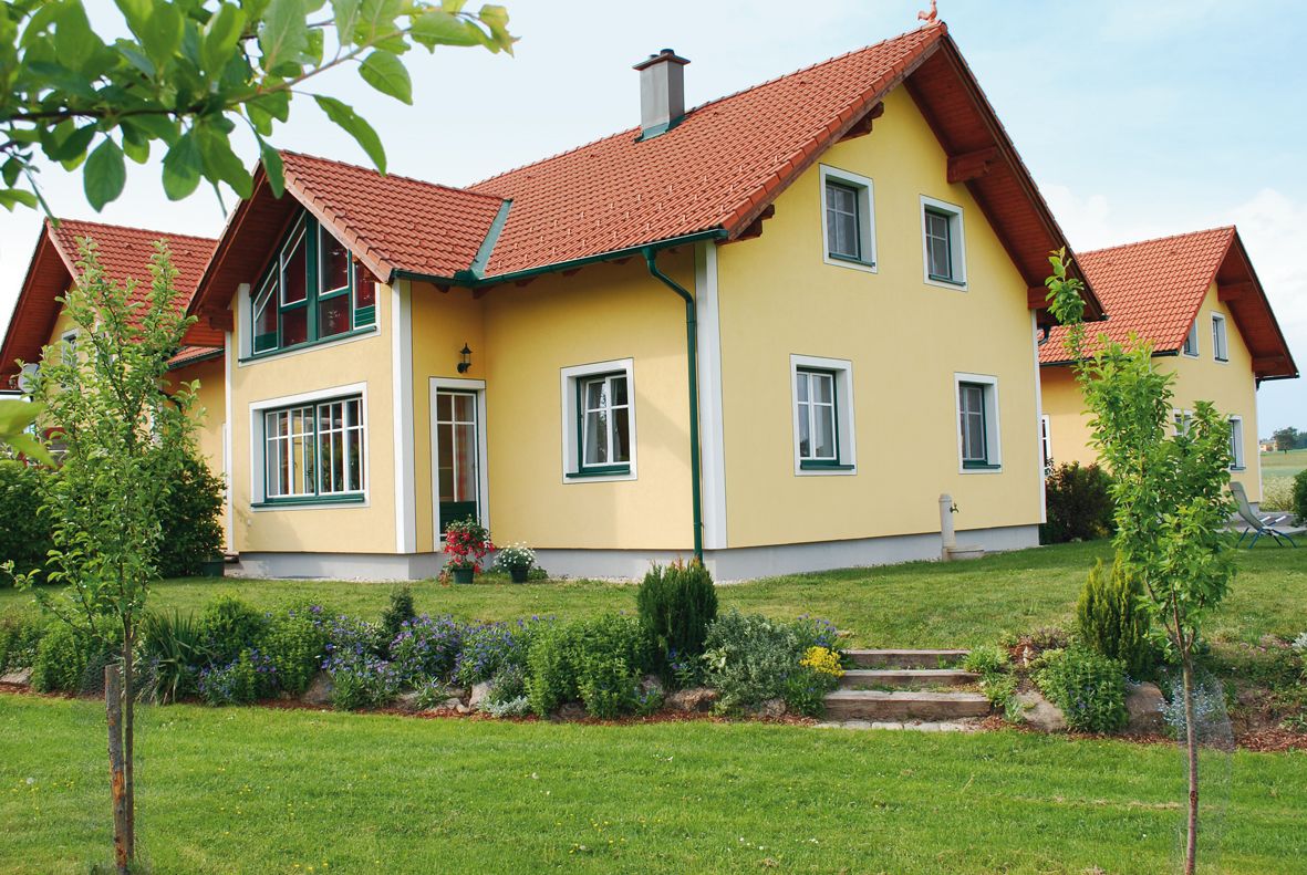 Gelbes Einfamilienhaus mit rotem Dach und gepflegtem Garten.
