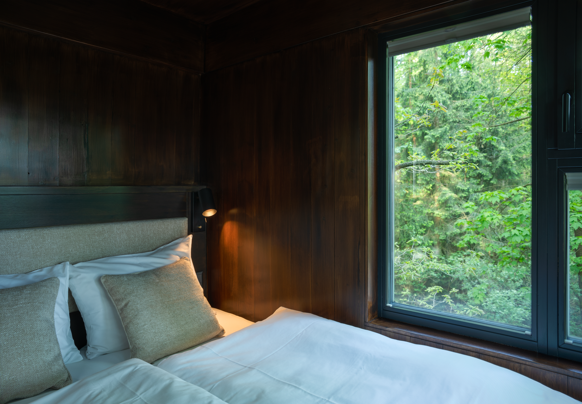 Interior view of a tree house with a bed and a window overlooking the forest.
