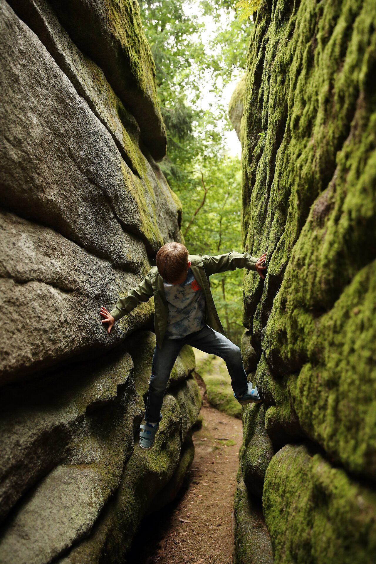 Ein Kind versucht zwischen zwei großen Felsblöcken hoch zu klettern. 