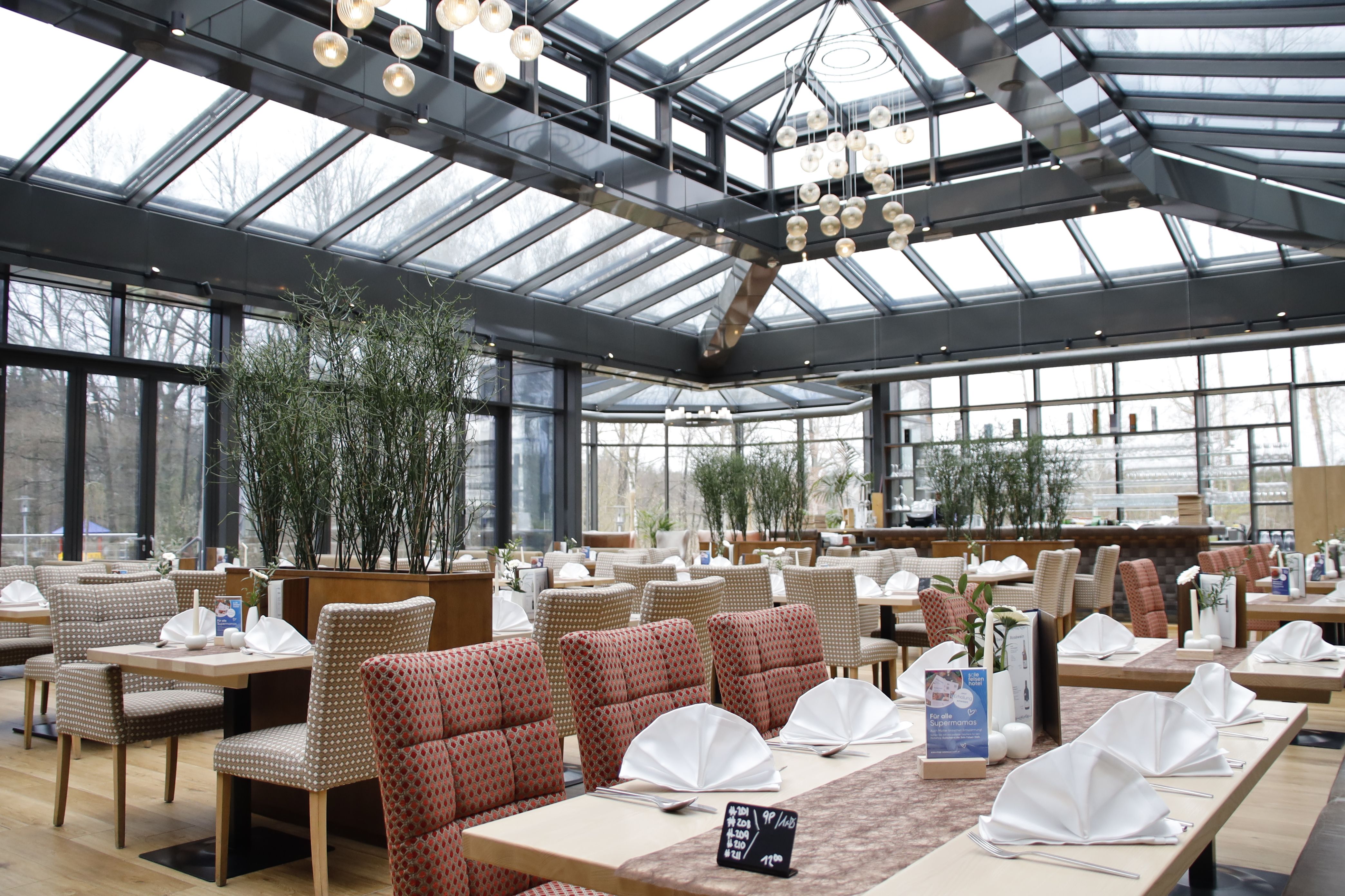 Innenansicht eines modernen Restaurants mit Glasdach und gedeckten Tischen.