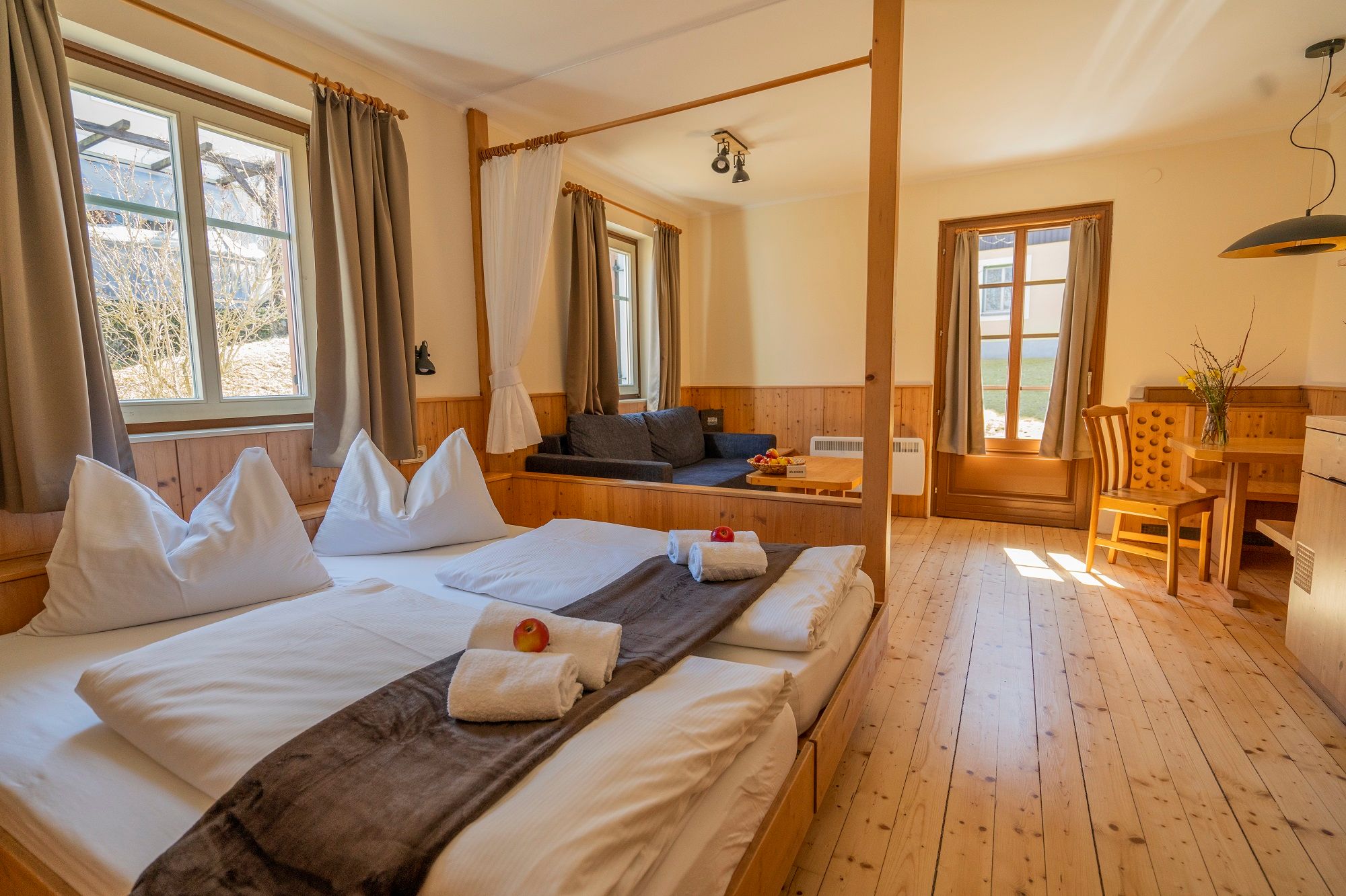 Gemütliches Zimmer mit Doppelbett, Sofa, Esstisch und großen Fenstern im Theater- und Feriendorf Königsleitn.