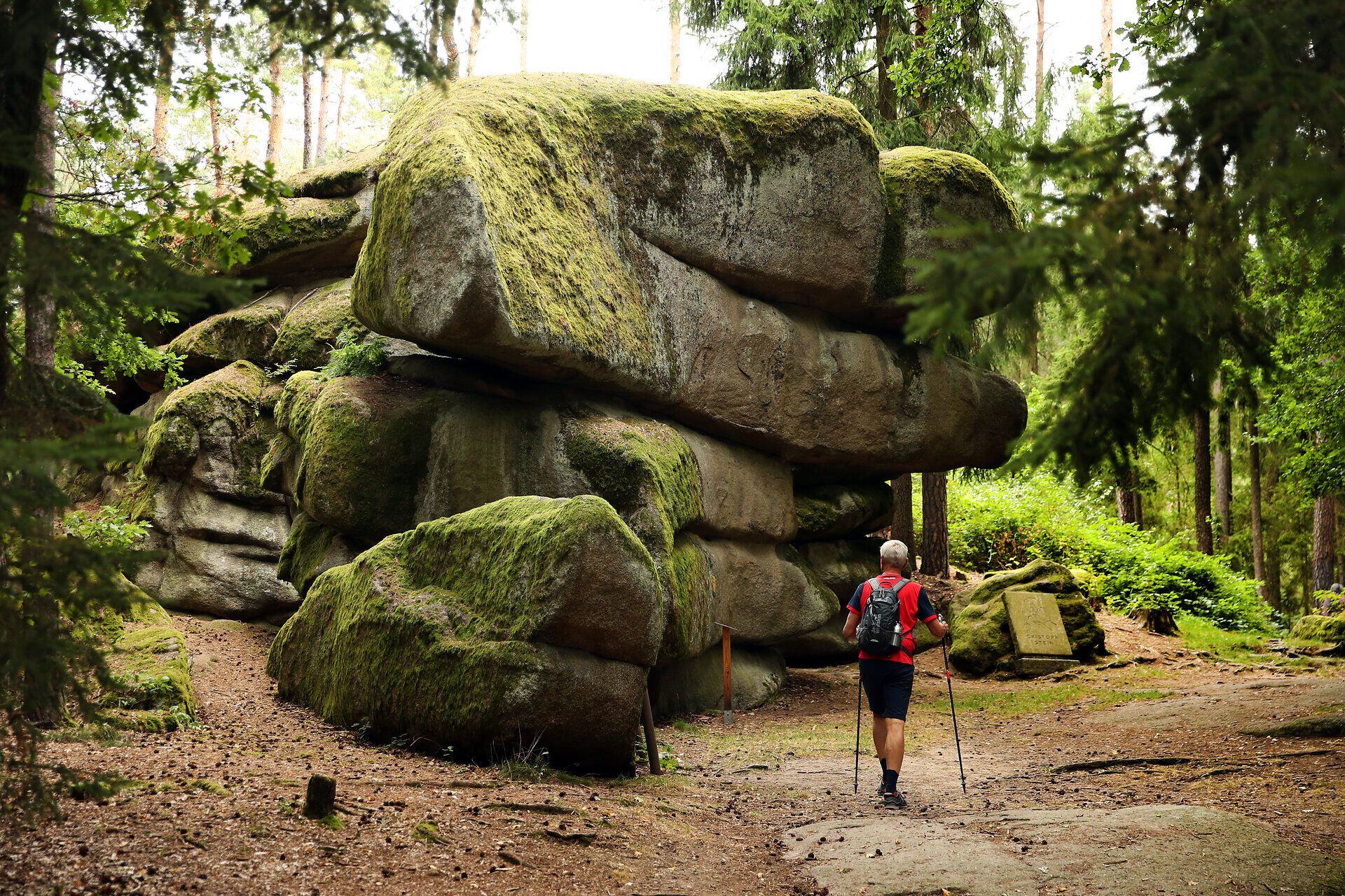 Ein Mann wandert neben einer großen Felsformation entlang eines Wanderweges. 