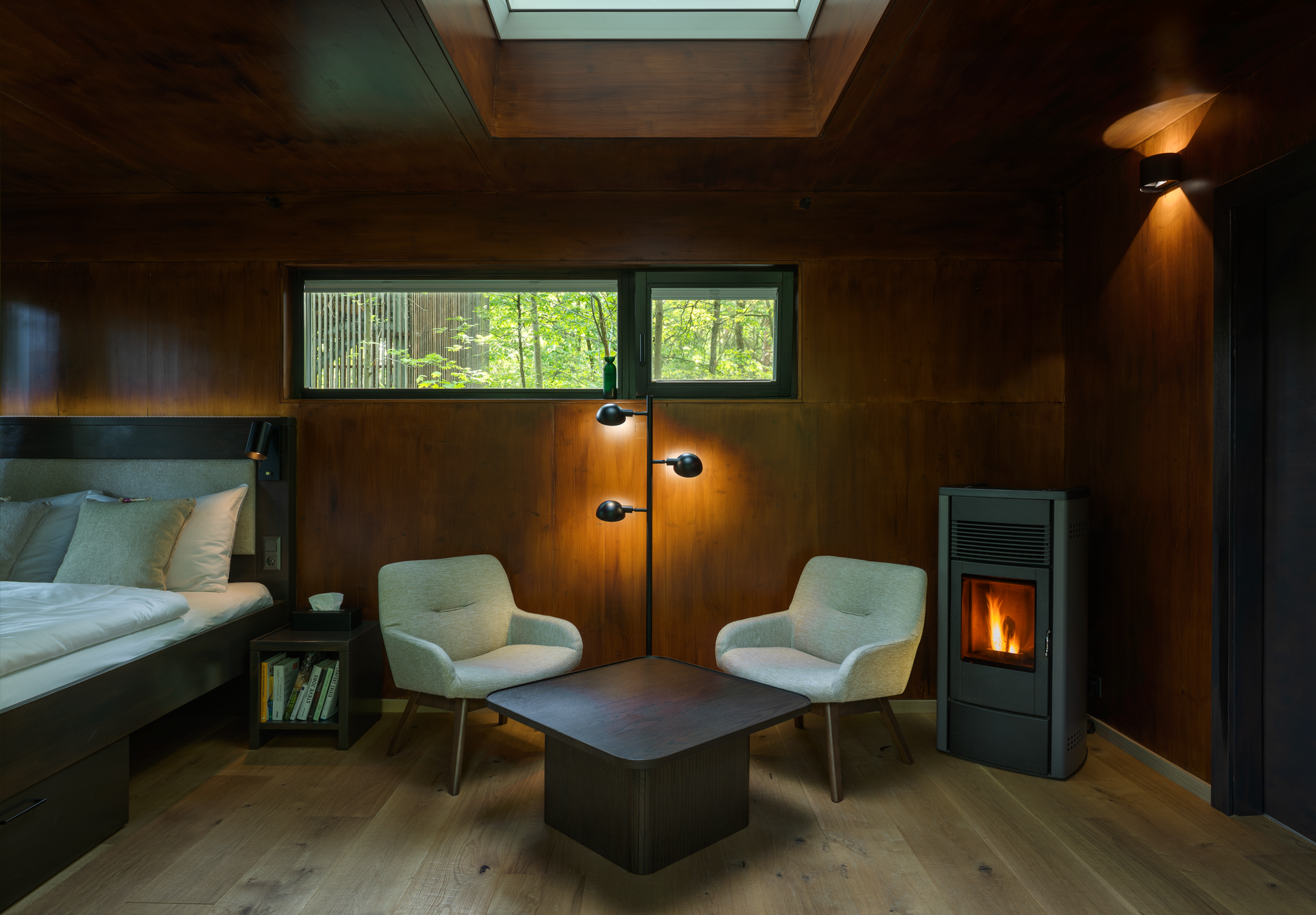 Interior view of a cozy tree house with wooden paneling, two armchairs, a table and a fireplace.